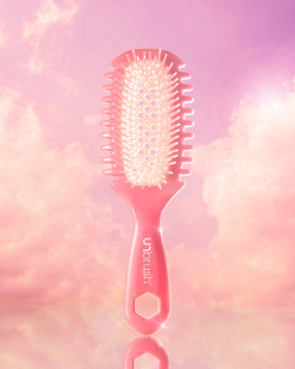 Pink hairbrush with 'Unbrush' branding on a soft pink and purple gradient background