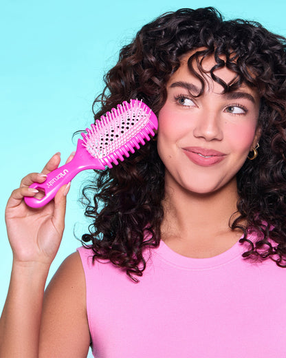 Woman with curly hair holding a pink hairbrush against a blue background