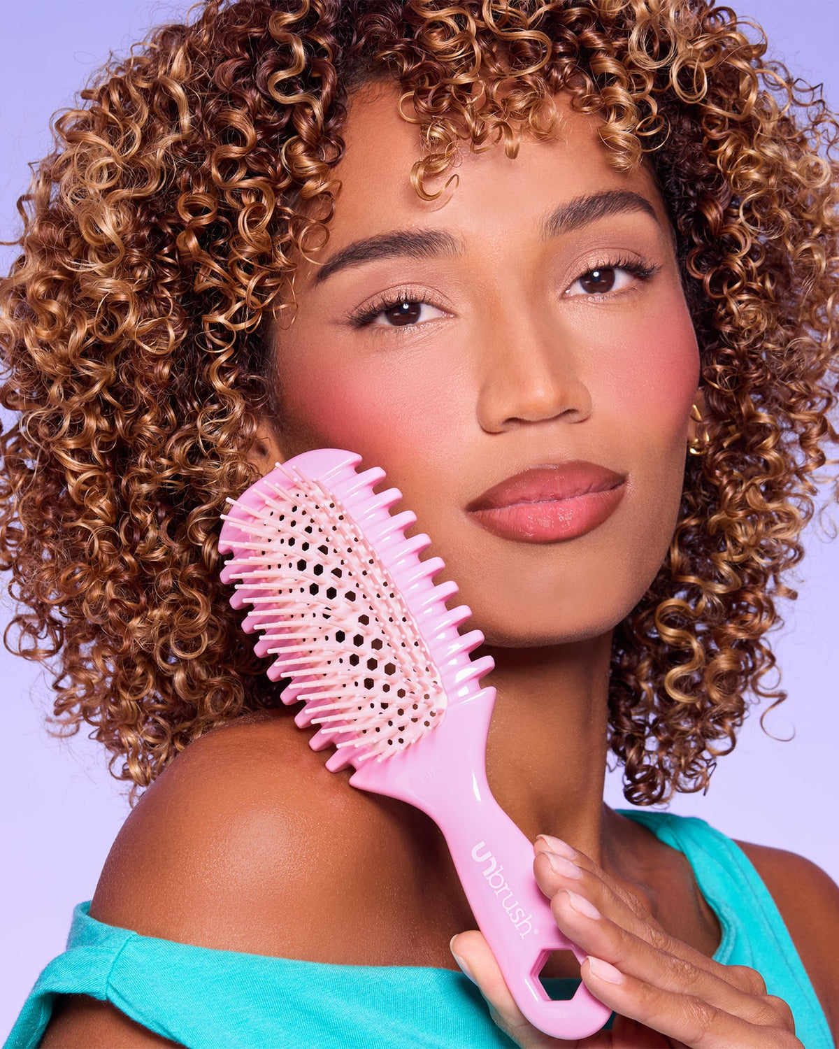 Woman with curly hair holding a pink hairbrush against a purple background