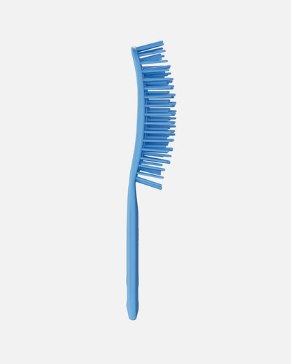 Side view of a blue UNbrush hairbrush showing its curved shape and flexible bristles, on a off-white background.