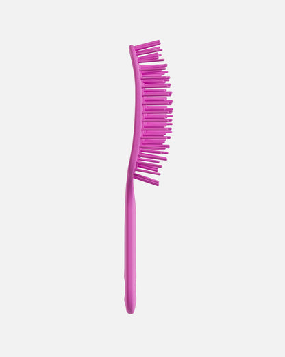 Side view of a pink UNbrush hairbrush showing its curved shape and flexible bristles, on a off-white background.