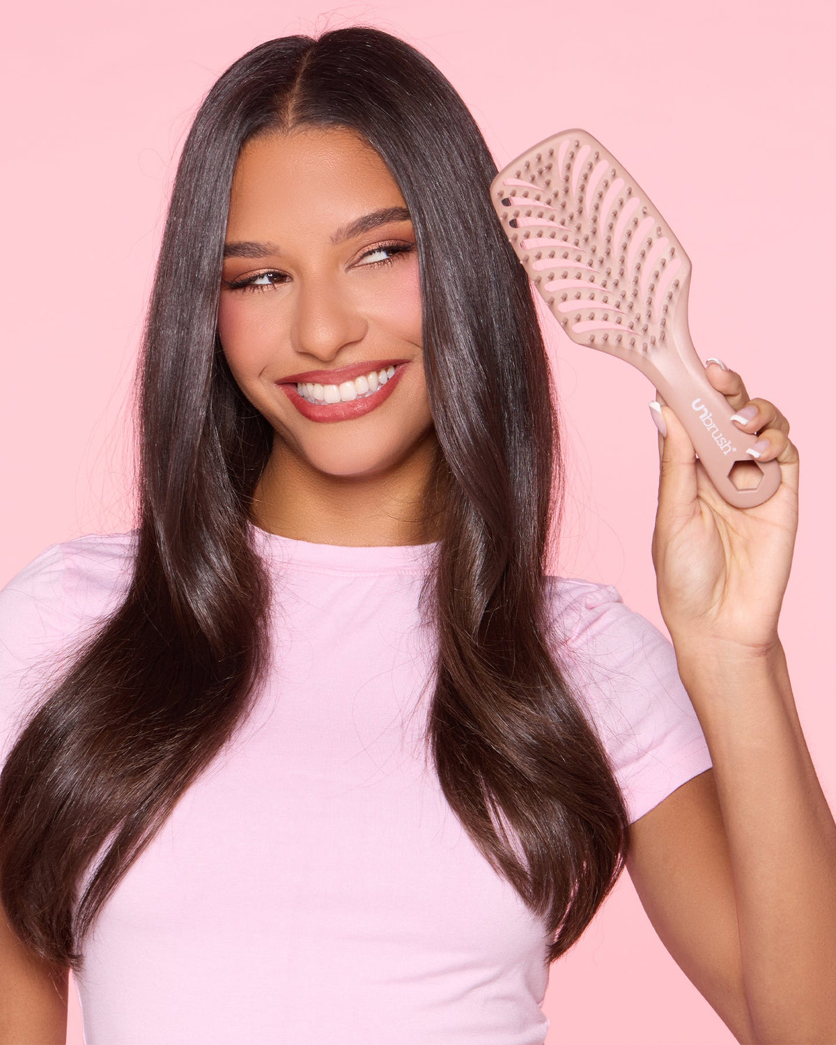 Woman with long hair holding a hairbrush against a pink background