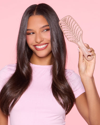 Woman with long hair holding a hairbrush against a pink background