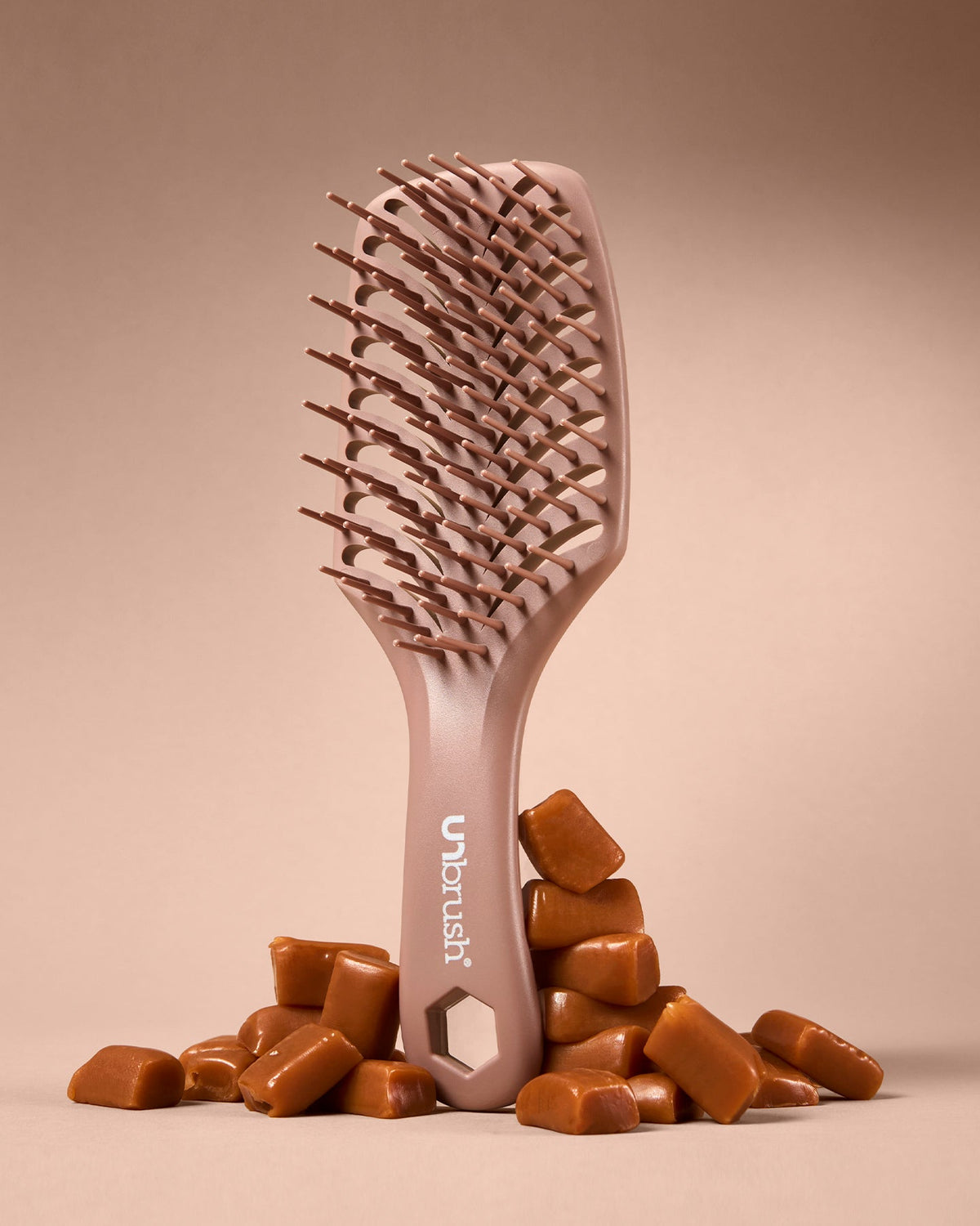 Hairbrush with 'Ubrush' branding on a beige background with caramel candies.
