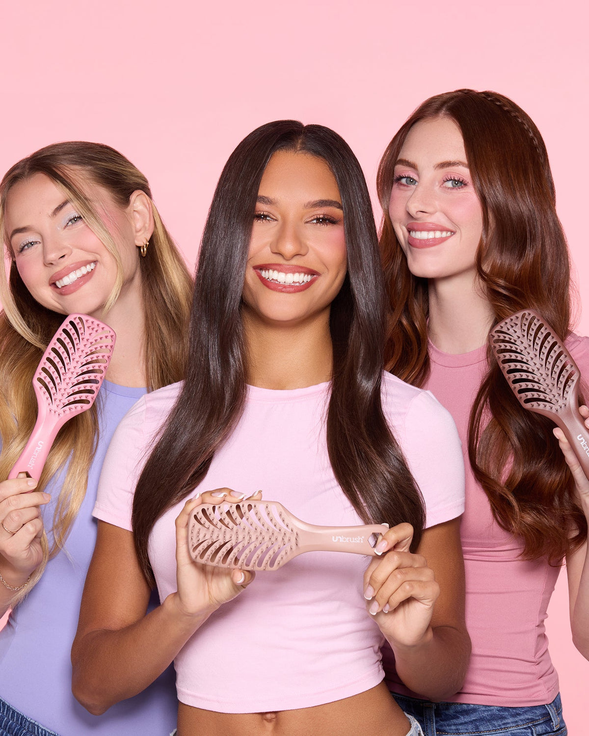 Three women holding hairbrushes against a pink background