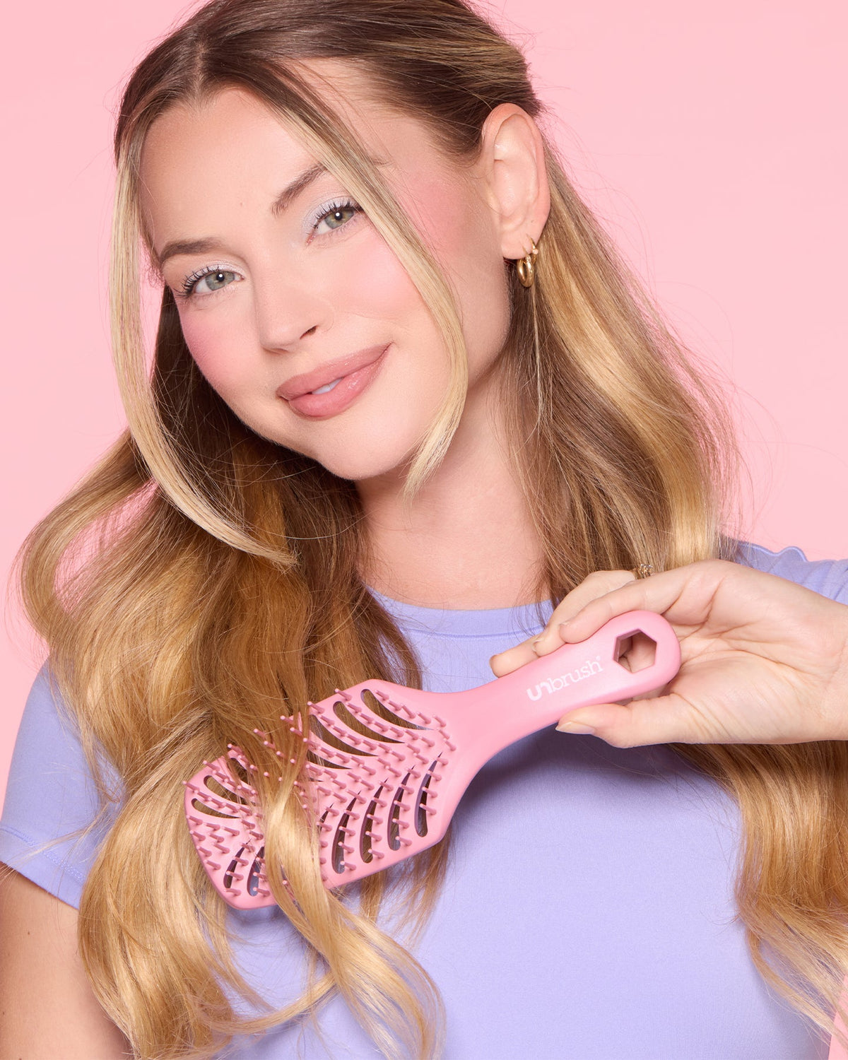 Woman holding a pink hairbrush against a pink background