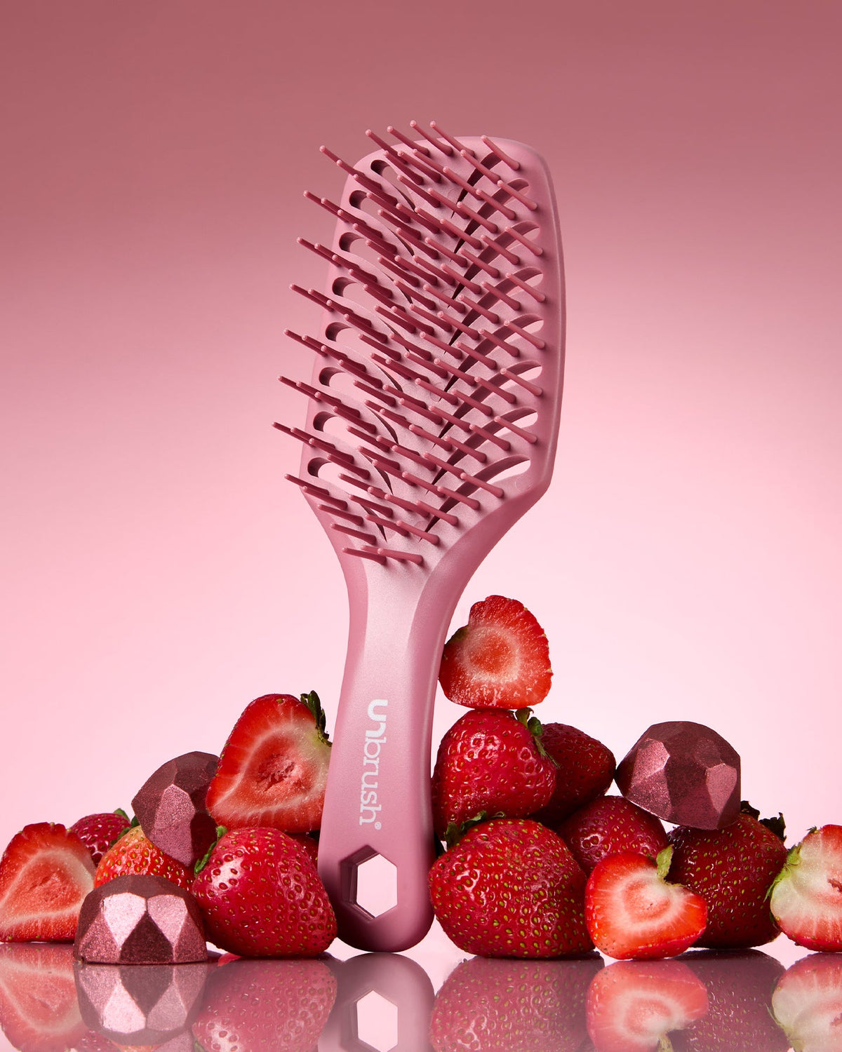 Pink hairbrush with 'Ubrush' branding on a pink background with strawberries and red stones.